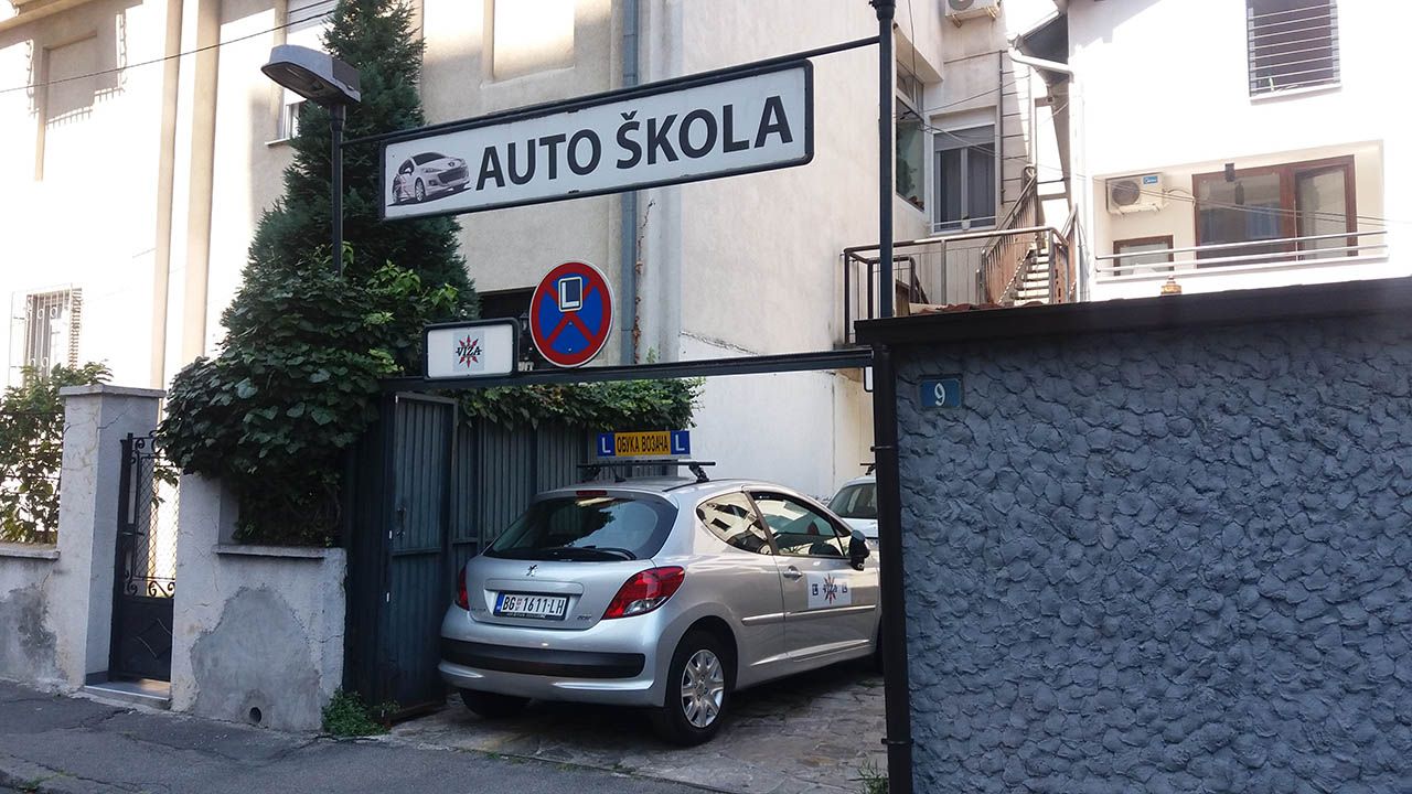 Ulaz u Auto školu Viza: tabla „Auto škola” iznad kapije i vozilo škole parkirano ispred